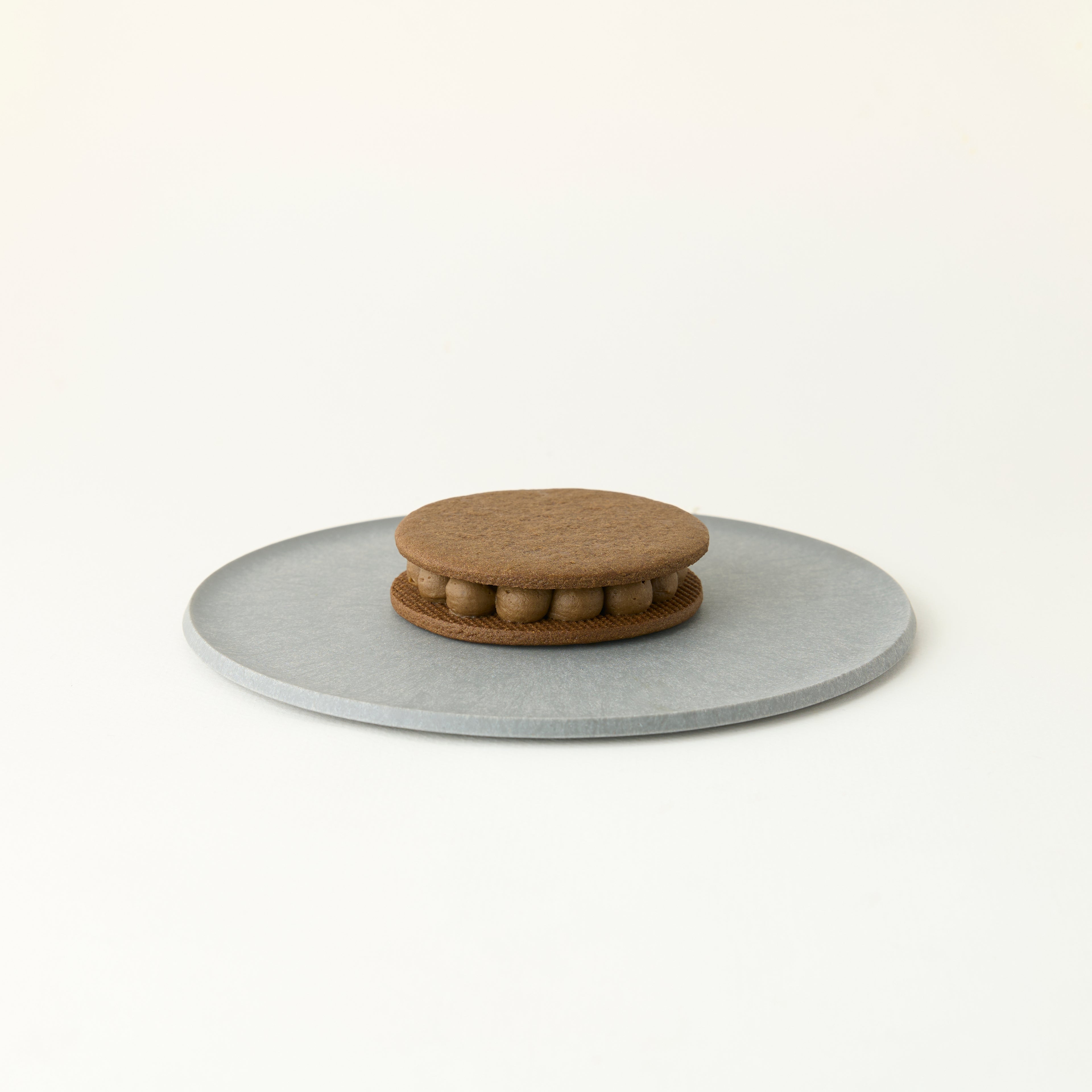 Round gray stone coaster with a Hojicha biscuit on top on a white background