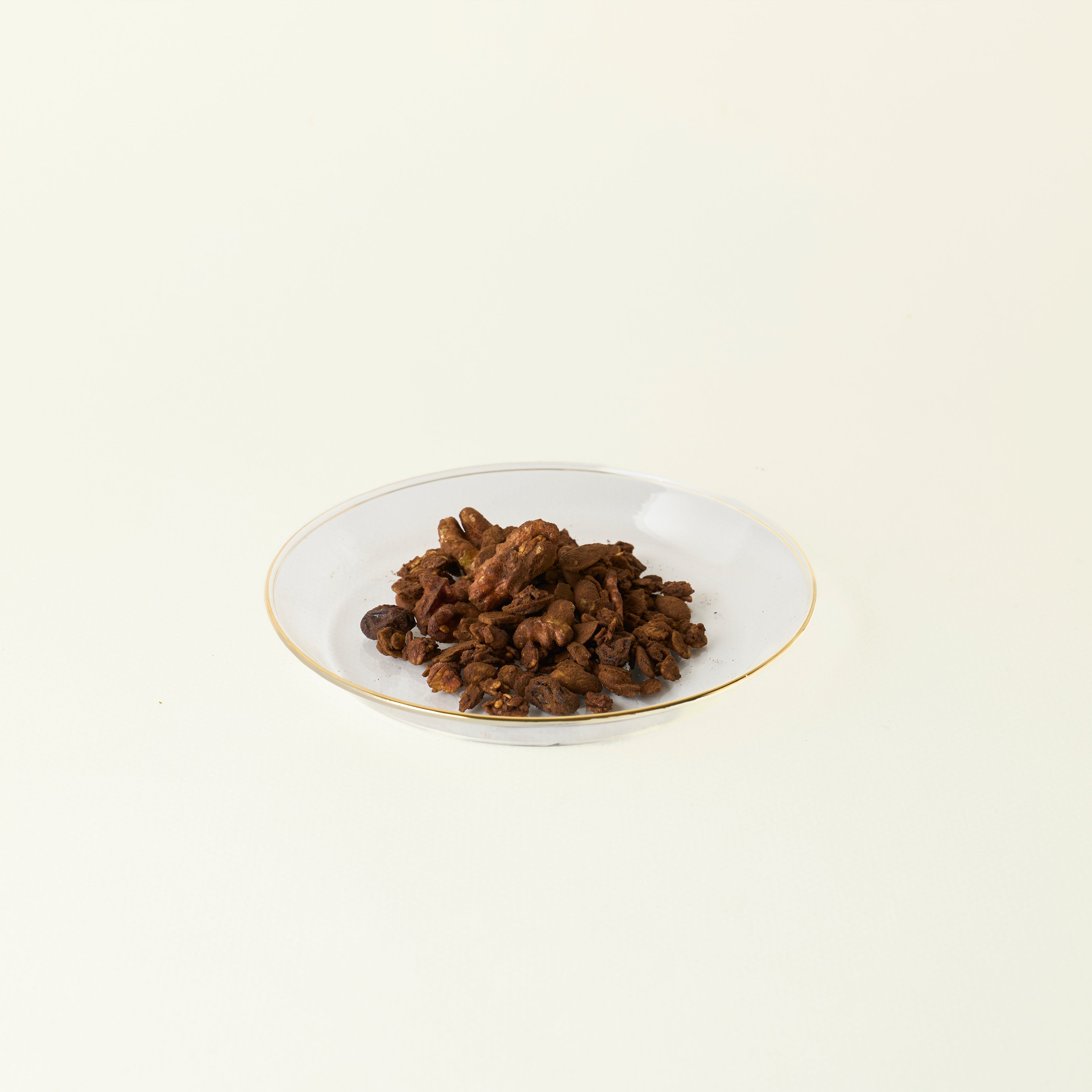 MATCHADO Vegan Hojicha Granola - Great Taste Award Winner - Sugar-Free & Nutty Roasted Aroma. White plate with a small amount of dark brown food on a light beige background.