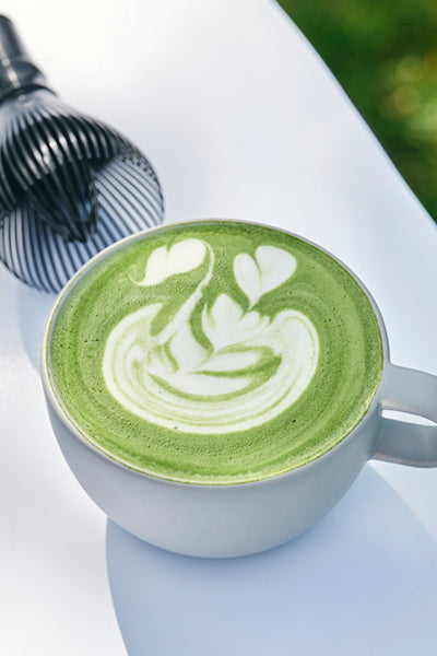 MATCHADO Kyushu Saemidori Matcha.  MATCHADO Matcha latte art in a white cup on a white surface with a blurred background