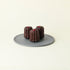 Three Chocolate Canelés on a grey plate, topped with dried raspberries and gold leaf. The dark, caramelized crust reflects a MATCHADO twist on the classic French pastry.