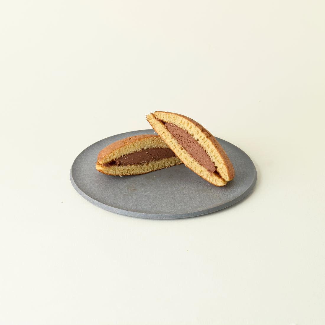 MATCHADO Miffy chocolate Dorayaki - Authentic Japanese Pancake - Fluffy &amp; Sweet Handmade Treat. Two halves of a dorayaki with chocolate filling on a gray plate against a beige background