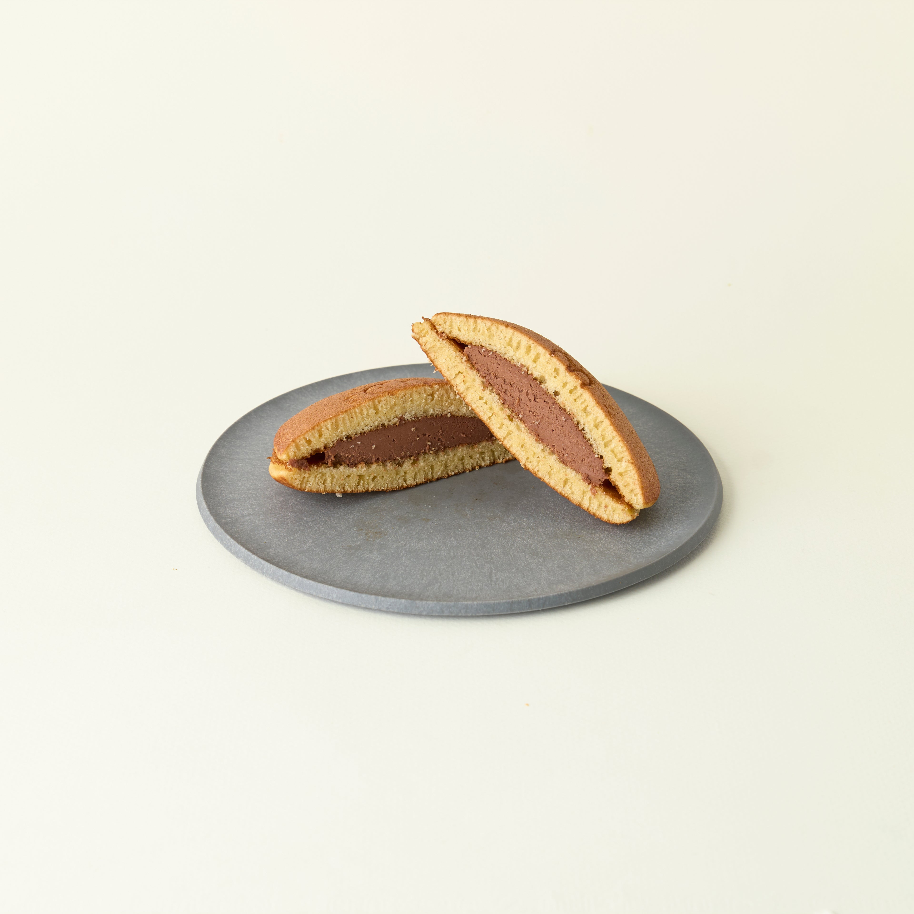 MATCHADO Miffy chocolate Dorayaki - Authentic Japanese Pancake - Fluffy &amp; Sweet Handmade Treat. Two halves of a dorayaki with chocolate filling on a gray plate against a beige background