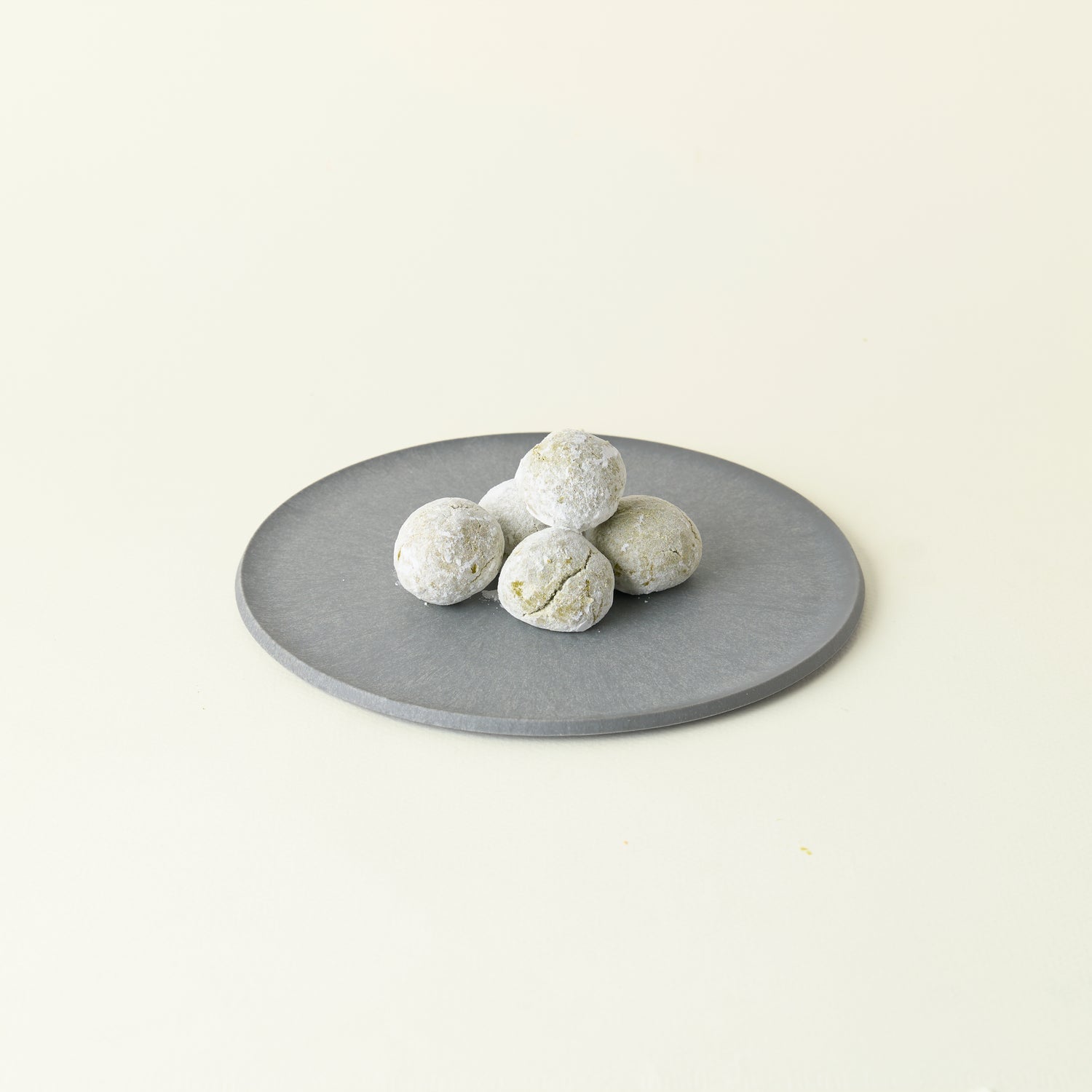 MATCHADO Vegan Boule de Neige Biscuits - Matcha or Strawberry Flavour. Round gray stone on a light beige background
