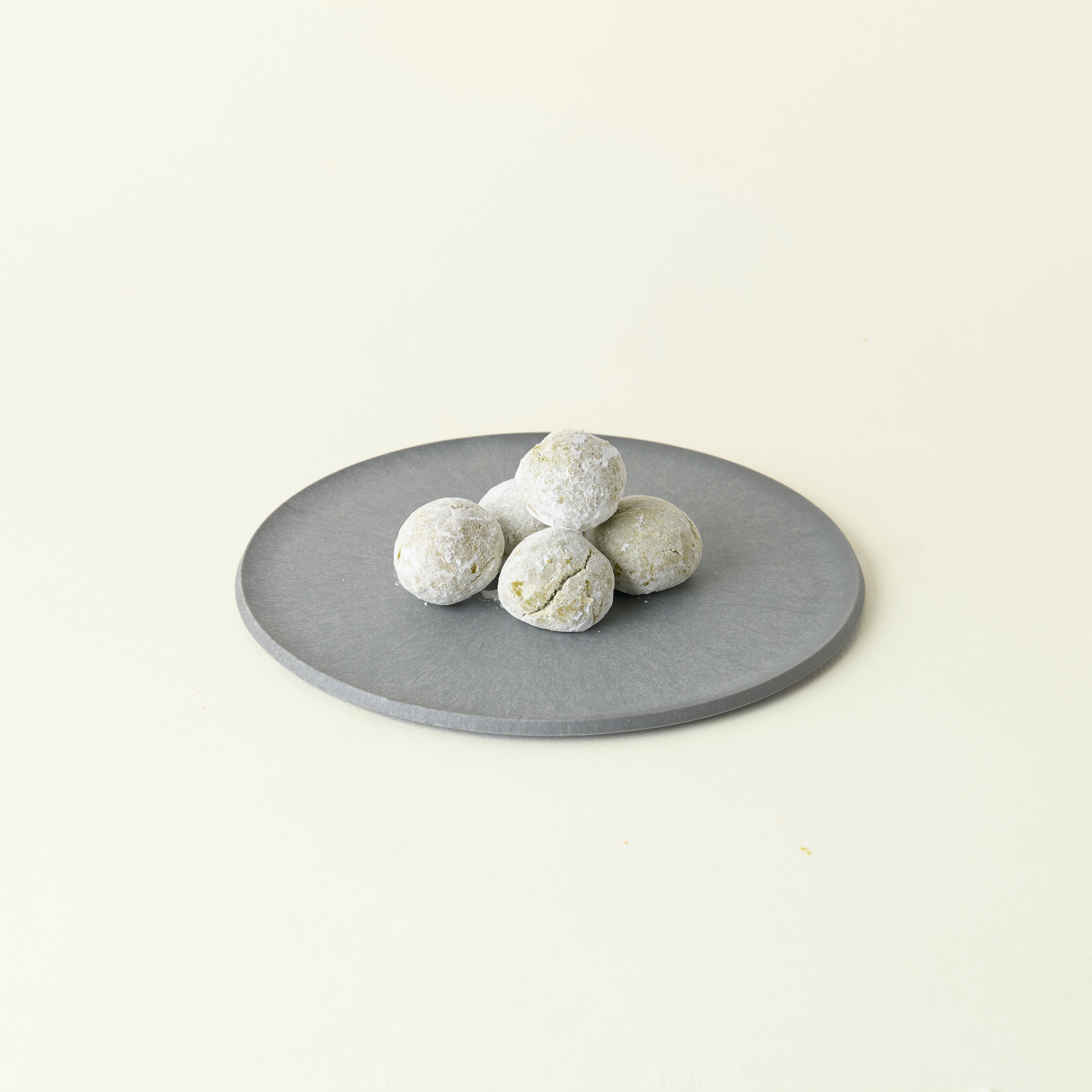 MATCHADO Vegan Boule de Neige Biscuits - Matcha or Strawberry Flavour. Round gray stone on a light beige background
