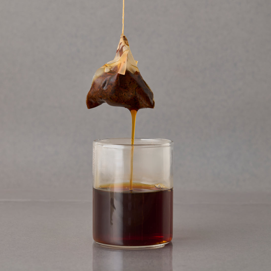 MATCHADO Nara Natural Tea - Wakocha Japanese Black Tea - Organic Pesticide-Free - Floral &amp; Honey Aroma. Tea bag being dripped into a glass of water on a gray background